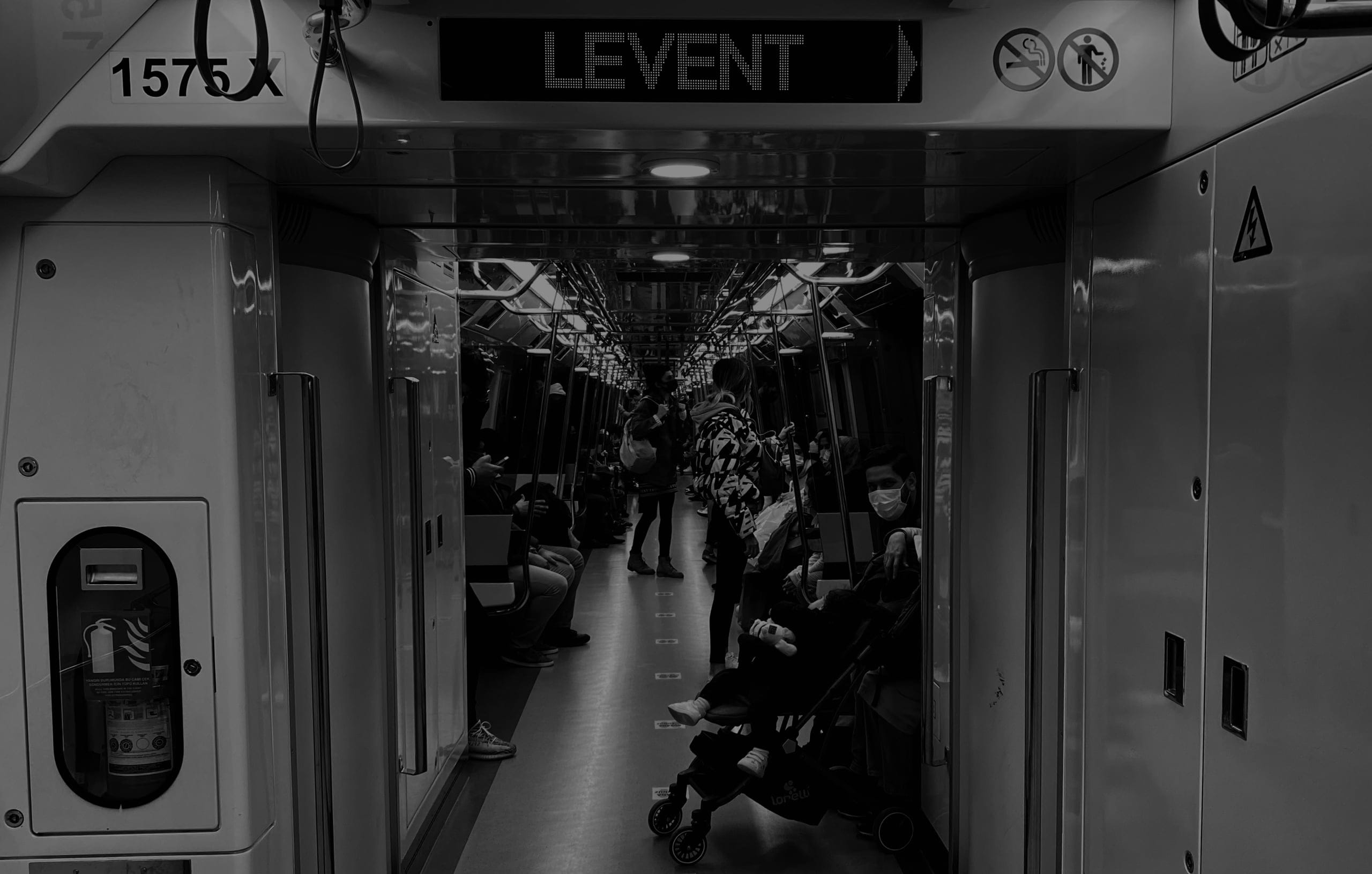 Metro vagonunun metal çerçeveleri arasında yolcular ve Levent yön tabelası; siyah-beyaz fotoğraf.