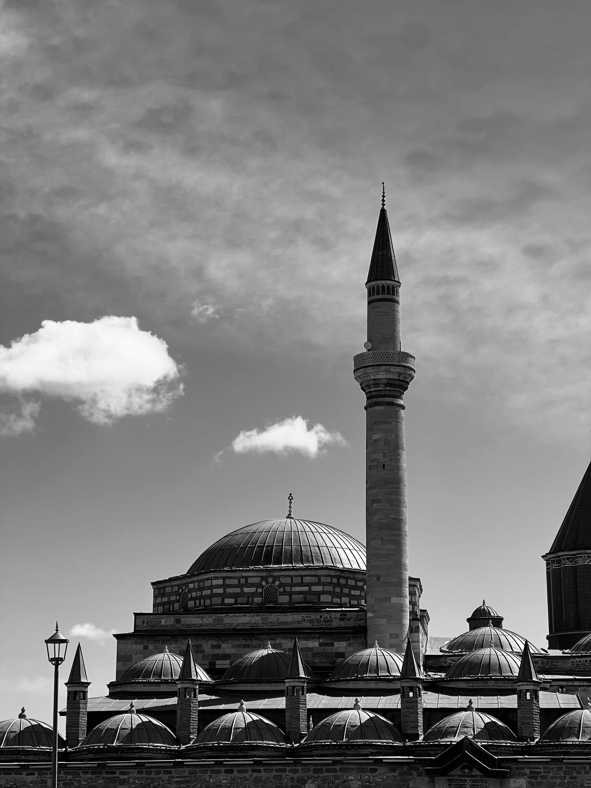 Bulutlu gökyüzünde cami kubbeleri ve ince bir minare; siyah-beyaz fotoğraf.